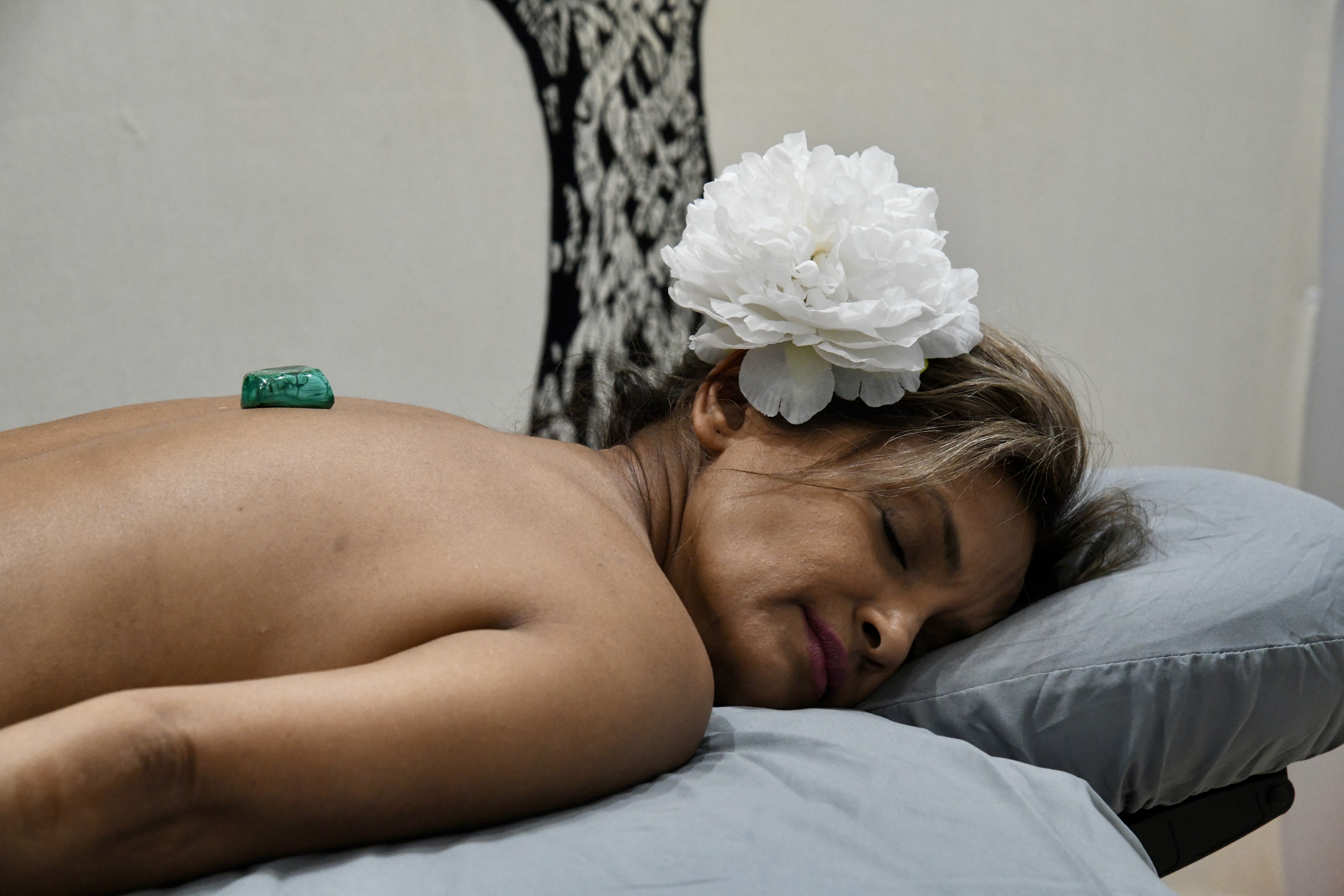 Woman lying down with white flower in her hair and malachite stone on her back