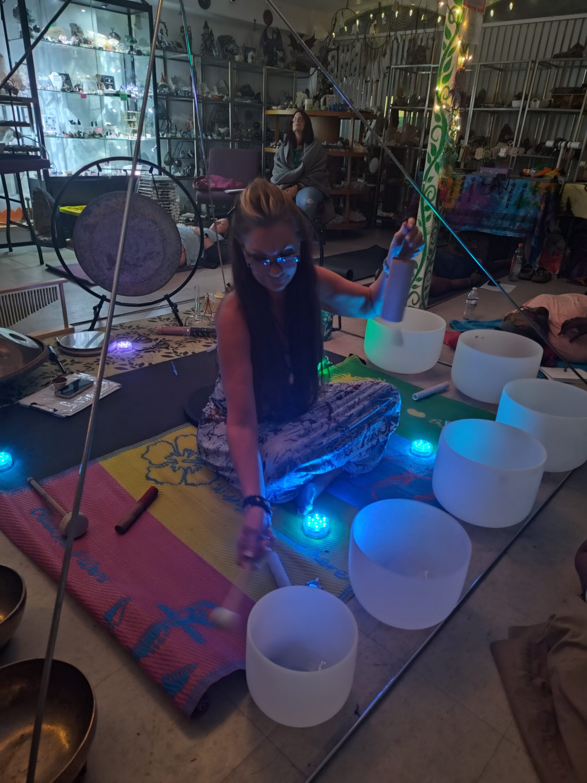 Woman sits on floor under a pyramid frame while striking frosted glass sound bowls