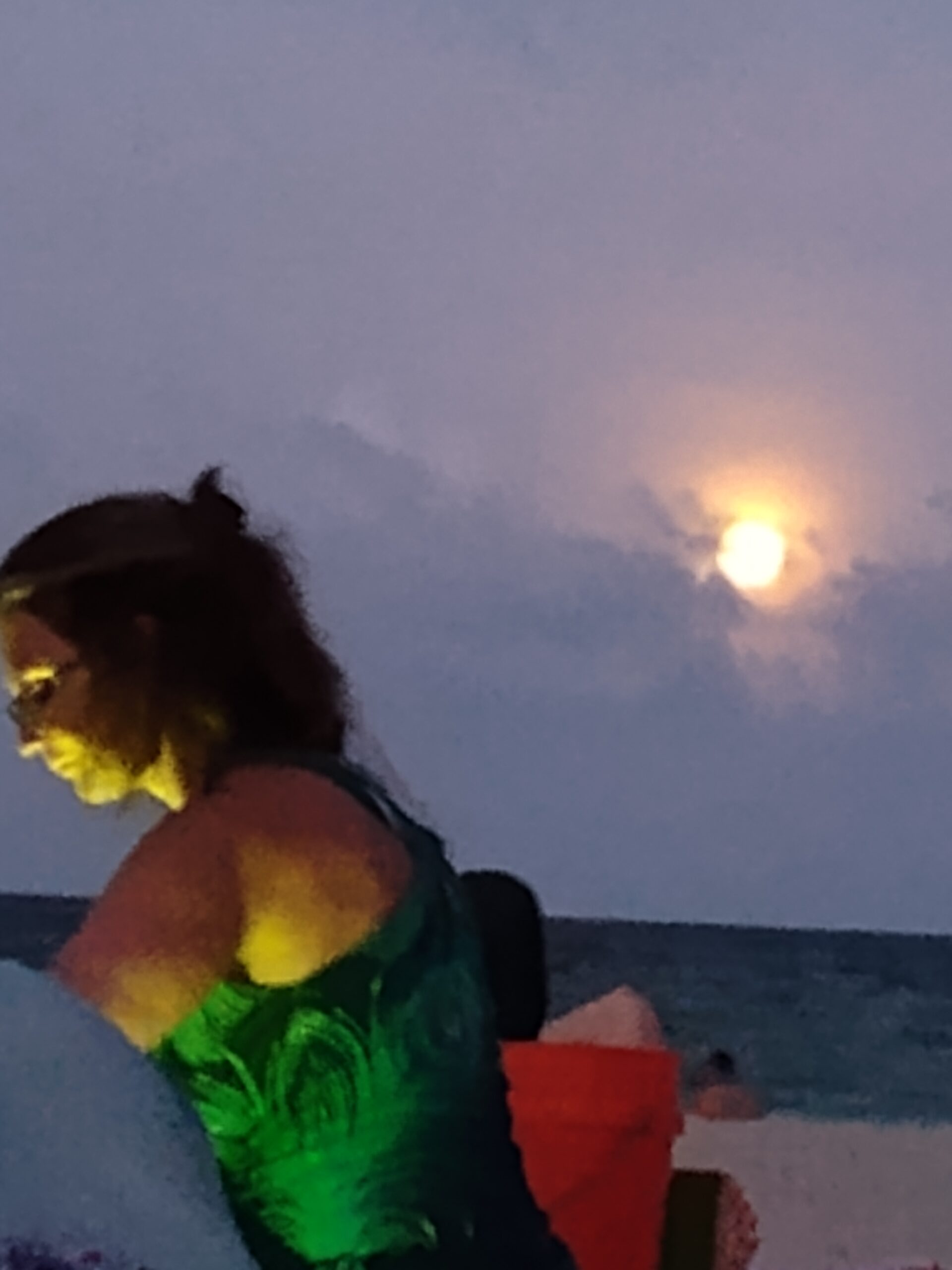 Woman in green dress standing on a beach with a moon behind her