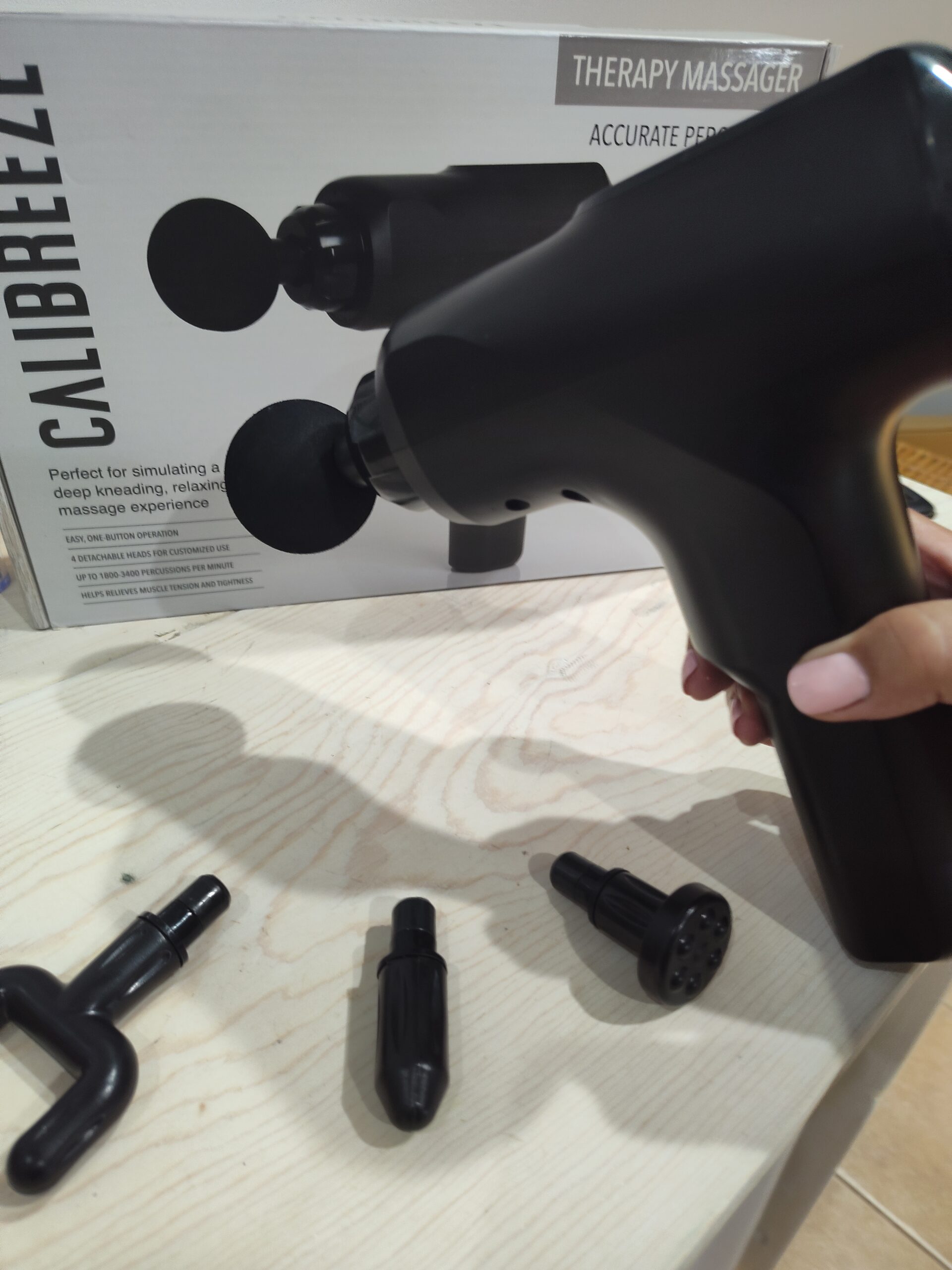 Right hand holding Calibreeze Self Massage Gun with 4 attachments visible