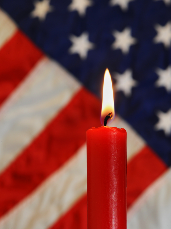 Lit red candle in front of a portion of the US Flag