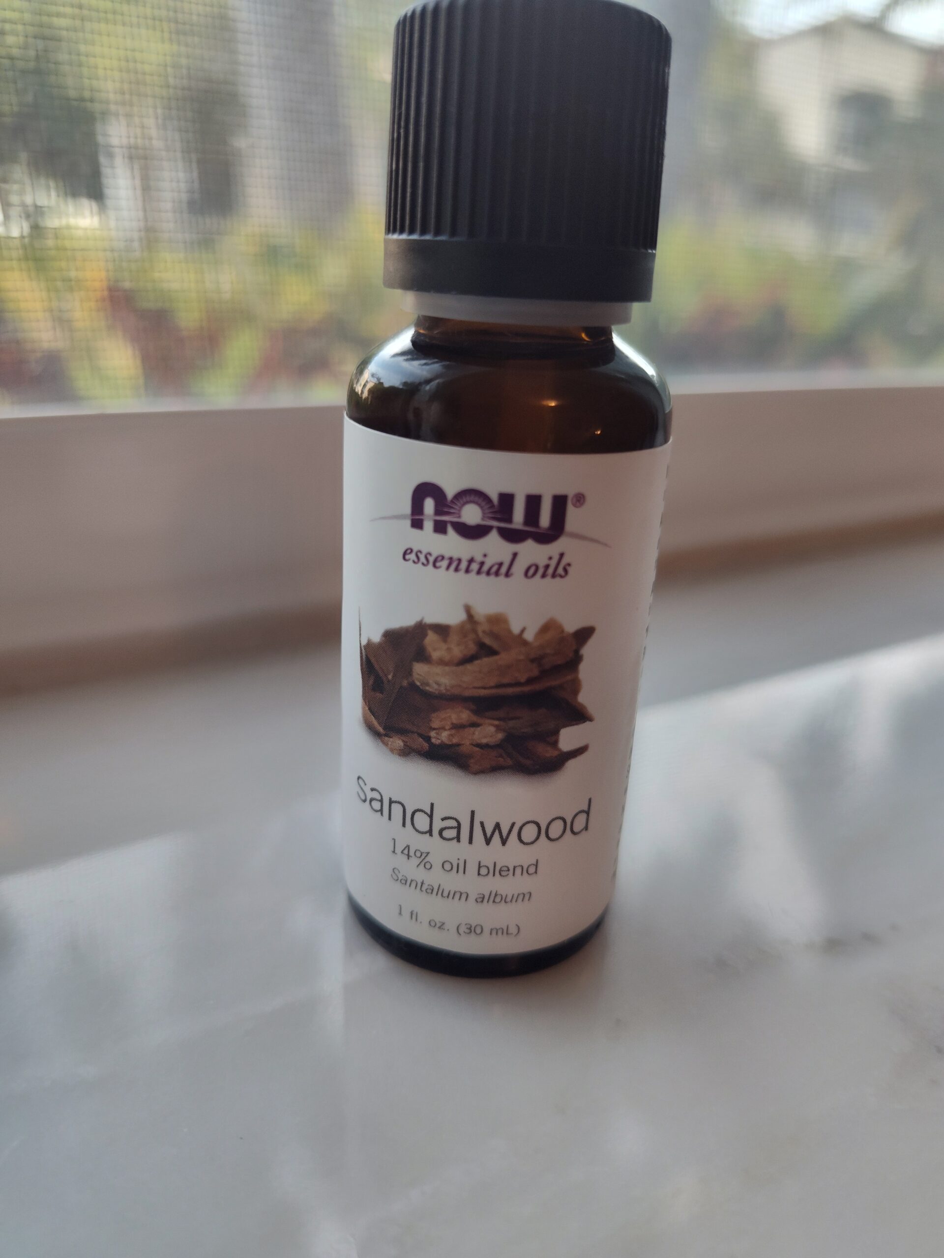 Bottle of NOW sandalwood essential oil on a windowsill