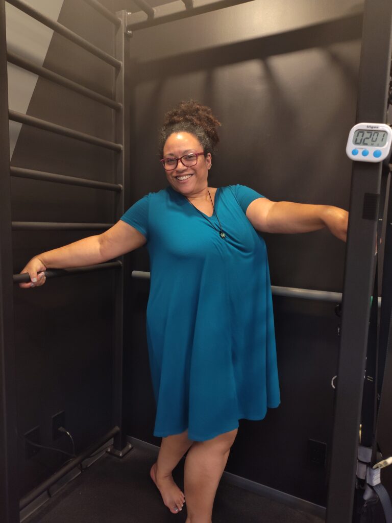 April in a teal dress posing on OsteoStrong's Vibe Plate