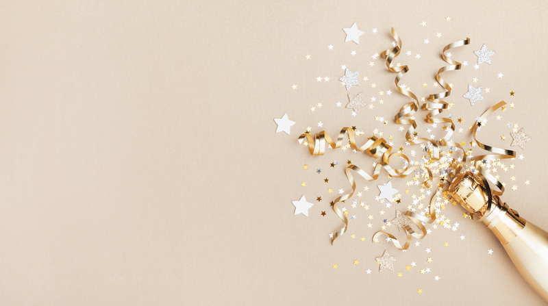 Pale golden background with metallic confetti popping out of a champagne bottle