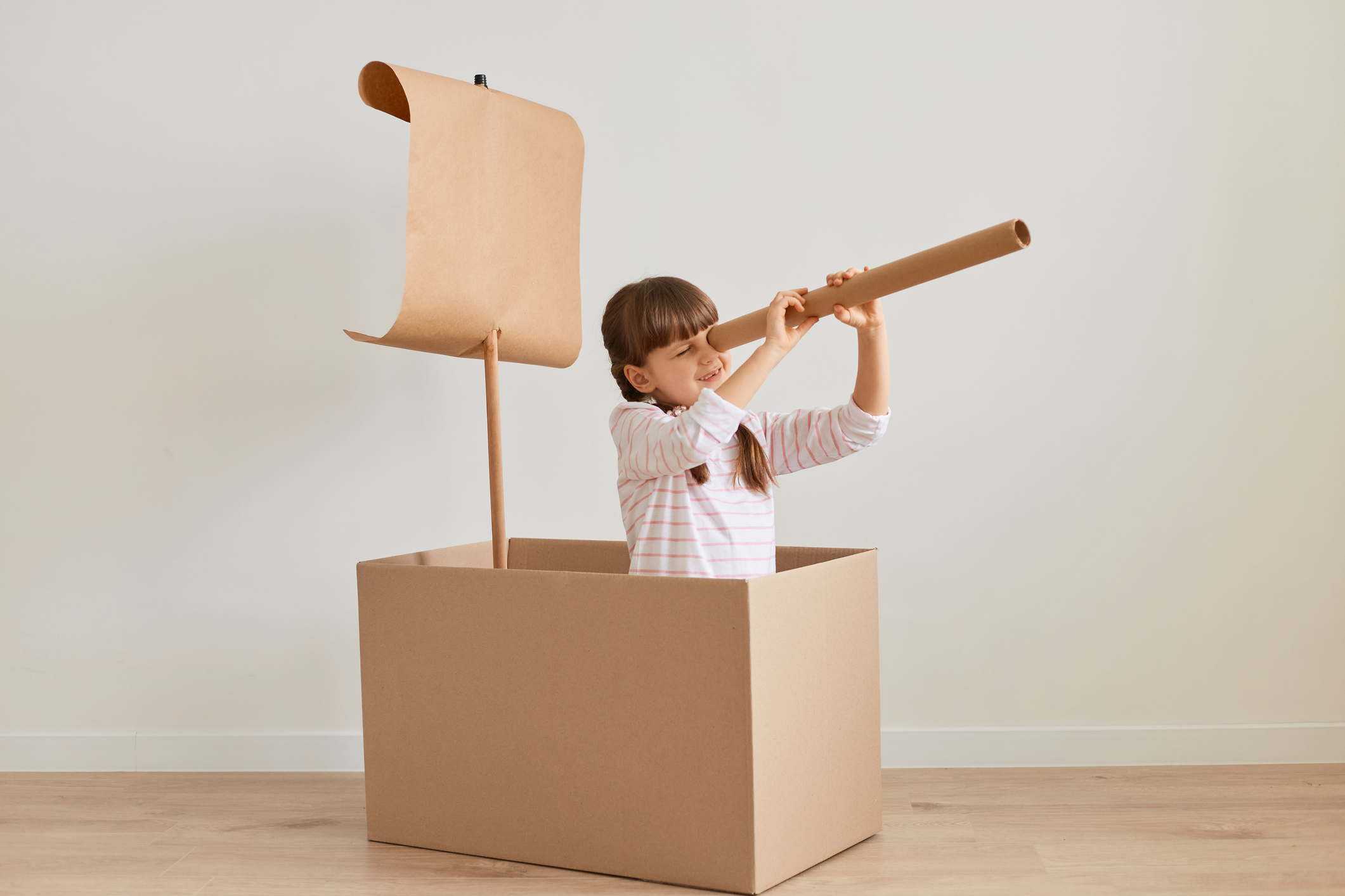 Young girl looking through a telescope in a cardboard boat.